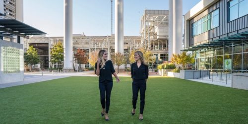 Dr. Kimberley Barclay walking through the courtyard at the office building location of Toothbar Austin, TX downtown dentistry. Smiling and looking at one another, Dr. Lauren Jacobsen is to the right.