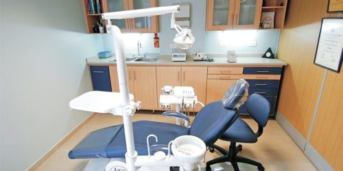 A dental office with a patient chair, dental tools, and a light. The office is clean with a diploma hanging on the wall.