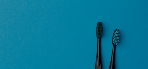 A blue background with two black toothbrushes on the right side of the image where each toothbrush has colored pixels. The image is a web banner used to hold text that goes over it as marketing messages.
