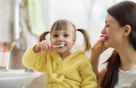 Mommy and daughter gently brushing teeth together in the bathroom