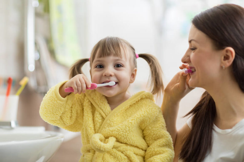 Mommy and daughter gently brushing teeth together in the bathroom