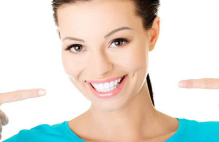Woman with white teeth smiling and pointing at her smile