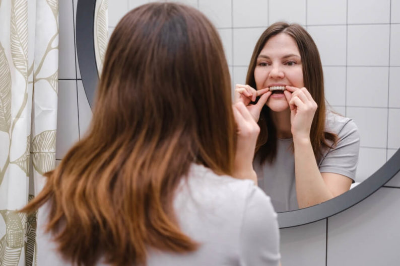 Woman in the bathroom placing invisalign braces after cleaning them