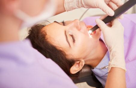 Cosmetic dentist looking at woman´s teeth with a light