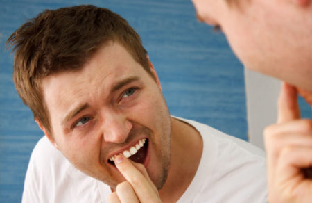 Man looking at the mirror while touching with his index finger a loose tooth in his upper teeth