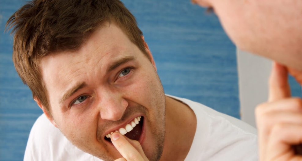Man looking at the mirror while touching with his index finger a loose tooth in his upper teeth