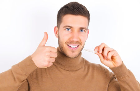 Man holding his invisalign retainer whiles smiling and giving a thumbs up on the other hand