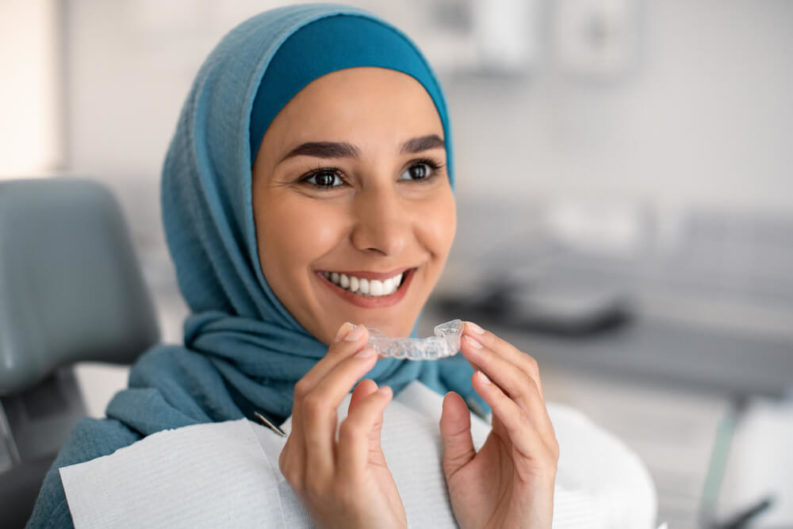 Woman smiling and holding her Invisalign aligner with both hands