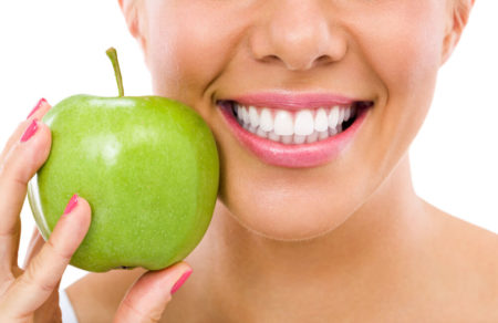 Woman with beautiful healthy white smile holding a green apple next to her face