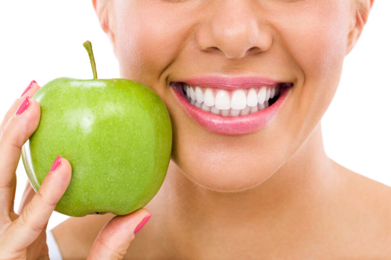 Woman with beautiful healthy white smile holding a green apple next to her face