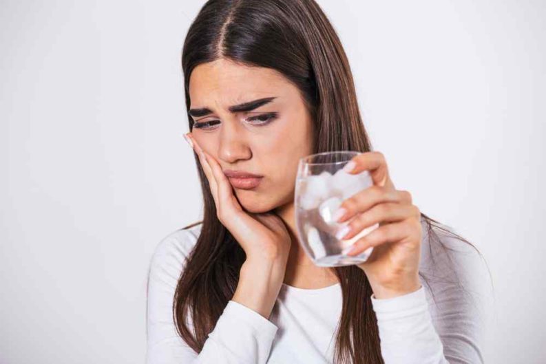Woman placing her hand on her cheek in tooth pain after having a drink of ice cold water